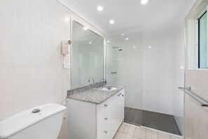 A modern bathroom with a glass shower enclosure, a white toilet, and a granite countertop sink. - Costa Unit 1 | 3 Bedroom Beachfront Apartment (Trinity Beach)