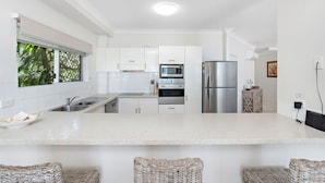 A modern kitchen with white cabinetry, stainless steel appliances, and a large island. - Costa Royale 3 Bedroom Beachfront Apartment (Trinity Beach)