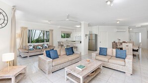 A spacious living area with wicker furniture, a dining set, and a kitchen in the background. - Costa Royale 3 Bedroom Beachfront Apartment (Trinity Beach)