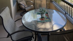 En balkon med et glasbord, stole og en potteplante.