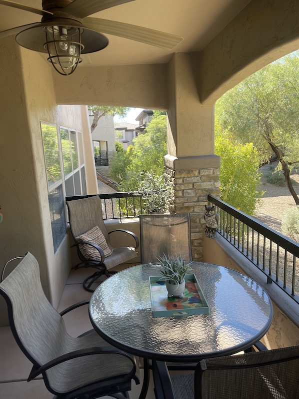 Un balcon avec une table en verre, des chaises et un pot de fleurs.