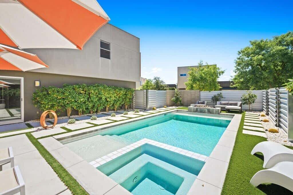 A modern outdoor swimming pool with a geometric design, surrounded by a well-maintained lawn and a patio area with outdoor furniture.