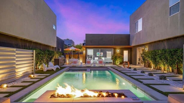 Ein moderner Poolbereich im Freien mit Feuerstelle, Liegestühlen und einer gut beleuchteten Terrasse.