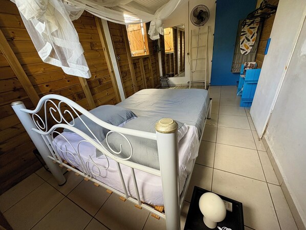 A wooden room with a bed, a fan, and a blue wall.