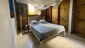 Un lit simple dans une pièce aux murs en bois et au sol carrelé.
