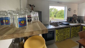 Une cuisine avec une fenêtre, un évier et une cuisinière. On y trouve des bocaux en verre sur le plan de travail et un saladier jaune.
