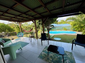 A covered outdoor area with a pool, chairs, and a hammock.