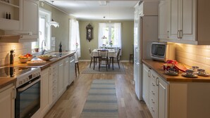 A kitchen with a central island, wooden cabinets, a dining table with chairs, and a television on the counter. - Hus vid Kjugekull (Fjälkinge)