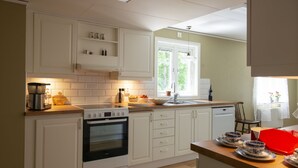 A modern kitchen with white cabinetry, a built-in oven, a coffee maker, and a window providing natural light. - Hus vid Kjugekull (Fjälkinge)