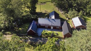 A rural property with multiple buildings, including a main house and several barns, surrounded by expansive green fields and a lake in the background. - Hus vid Kjugekull (Fjälkinge)