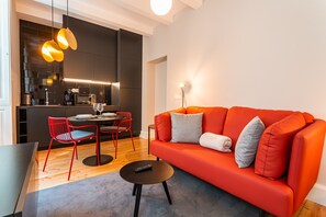 A modern living room with a red sofa, a round coffee table, and a dining area with red chairs.