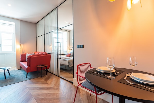 A modern hotel room with a dining area, a red sofa, and a glass partition separating the living and dining spaces.