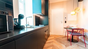 Una cocina moderna con microondas, hervidor de agua y cafetera. Hay una zona de comedor con mesa y sillas.