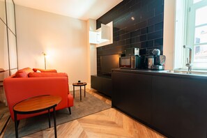 A modern kitchen with dark cabinetry, a microwave, and a coffee maker. There is a small round table and a red sofa in the living area.