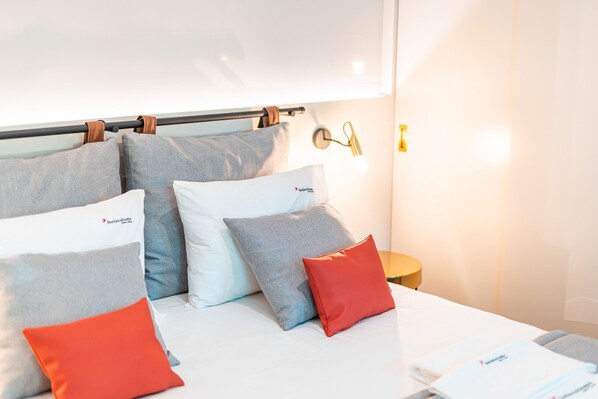 Une chambre d’hôtel avec un lit, des oreillers, une table de chevet et une lampe fixée au mur.