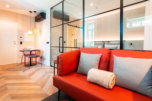 A modern room with a red sofa, a small dining table with red chairs, and a herringbone wooden floor.