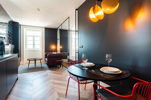 A modern dining area with a round table, red chairs, and a black tablecloth. There is a sofa and a small round table in the background. - FLH Viola Market Flat VI (Funchal)