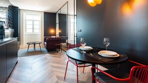 Ein moderner Essbereich mit einem runden Tisch, roten Stühlen und einer schwarzen Tischdecke. Im Hintergrund befindet sich eine Couch und ein kleiner runder Tisch.