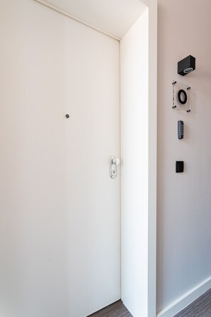 A modern hotel room with a white door, a keyhole, a wall-mounted control panel, and a small black device. - FLH Viola Market Flat VI (Funchal)