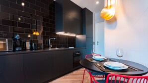 A modern kitchen with dark cabinetry, a built-in oven, and a dining area with a round table and red chairs. - FLH Viola Market Studio IV (Funchal)