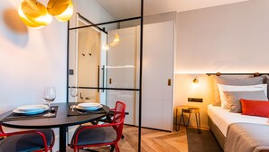 A modern hotel room with a bed, a small bedside table, a nightstand, and a dining area with a table and chairs. - FLH Viola Market Studio IV (Funchal)