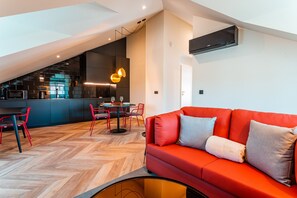 Un espace de vie moderne avec un canapé rouge, un parquet en bois à motifs chevrons, un coin cuisine et une table à manger avec des chaises rouges.