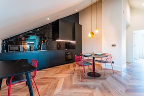 A modern kitchen with dark cabinetry, a herringbone wood floor, and a dining area with a black table and red chairs.