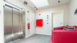 Habitación de hotel moderna con un amplio ventanal corredera, un extintor rojo, un armario rojo y un sofá rojo.