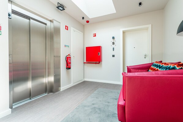 A modern hotel room with a large sliding door, a red fire extinguisher, a red cabinet, and a red sofa.
