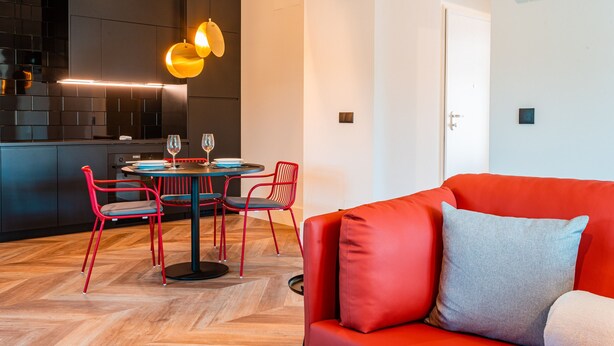 Un espacio moderno con un sofá rojo, una mesa de comedor con sillas y una zona de cocina.