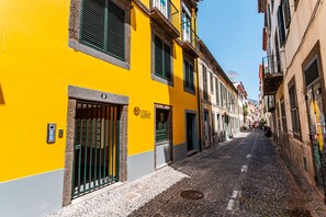 A narrow cobblestone street lined with yellow buildings, each with a distinct architectural style and visible doorways. - FLH Viola Market with Terrace I (Funchal)