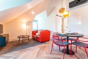 Una sala de estar moderna con un sofá rojo, una mesa de comedor redonda con sillas rojas y un piso de madera con diseño de espiga.