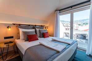 A hotel room with a large bed, a small table, a nightstand, and a view of the city through the window. - FLH Viola Market with Terrace II (Funchal)