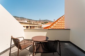 Un balcon avec deux chaises et une table, donnant sur un paysage urbain avec une colline et des bâtiments.