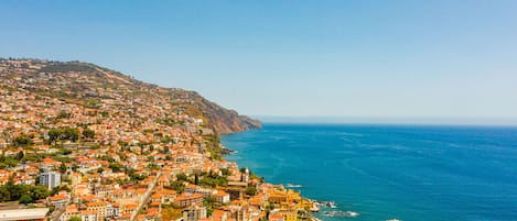 A coastal town with a dense cluster of buildings along the hillside and a beach area with a rocky shoreline.