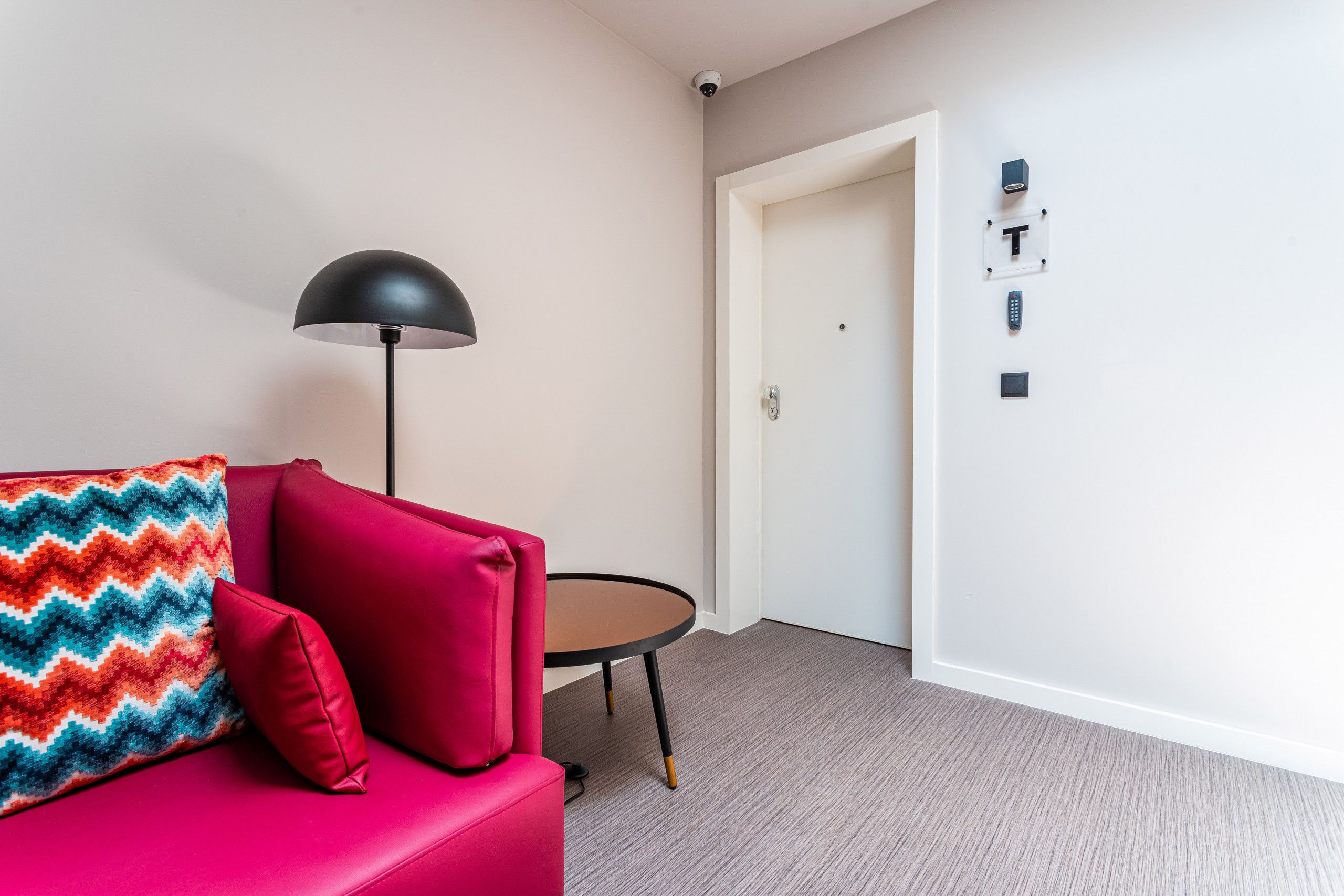 A modern room with a red sofa, a small round table, a black floor lamp, and a white door.