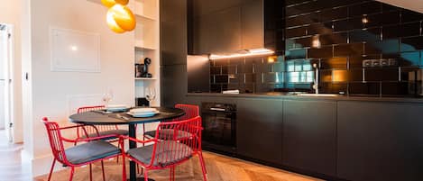 A modern kitchen with black cabinets, a built-in oven, and a dining area with red chairs and a round table.