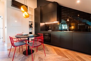 Una cocina moderna con armarios negros, horno empotrado y comedor con sillas rojas y una mesa redonda.