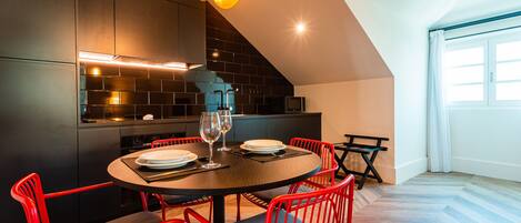 Cocina moderna con muebles oscuros, una mesa de comedor redonda, sillas rojas y una isla visible.