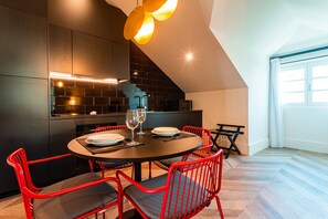 Cocina moderna con muebles oscuros, una mesa de comedor redonda, sillas rojas y una isla visible.