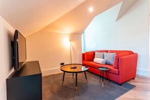 Un salon moderne avec un canapé rouge, une petite table ronde et un téléviseur à écran plat posé sur un meuble noir.