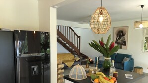 A modern kitchen with a black refrigerator, a central island with a fruit bowl, and a staircase leading to a living area with a blue sofa. - Villa with exceptional view of tropical garden! (Rivière-Salée)