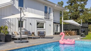 A swimming pool with a pink flamingo float, a white house with a balcony, and outdoor furniture.