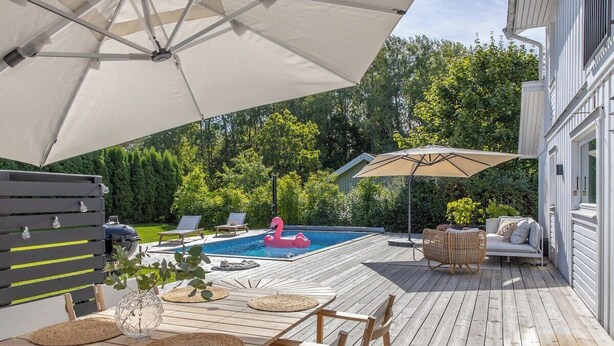 A wooden deck with a pool, lounge chairs, and a flamingo float.