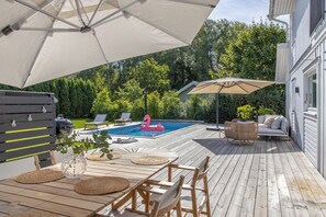 Una terraza de madera con piscina, sillas de descanso y un flotador con forma de flamenco.