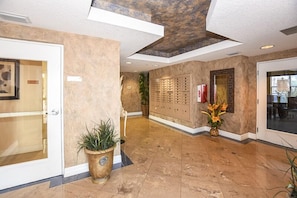 A lobby with a reception desk, a plant, a wall-mounted keycard dispenser, and a door. - Side Ocean View - Opus #402 (Daytona Beach Shores)