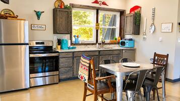A kitchen with a refrigerator, oven, microwave, and a dining table with chairs.