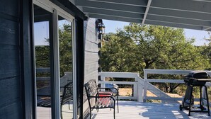 Una terraza techada al aire libre con puerta corrediza de vidrio, una parrilla metálica y un banco.