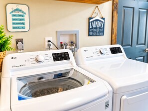 Une buanderie équipée de deux machines à laver LG blanches, d’un panneau indiquant les horaires de lessive et d’une affiche sur laquelle on peut lire : « La buanderie : on s’occupe de tout, une lessive à la fois. »