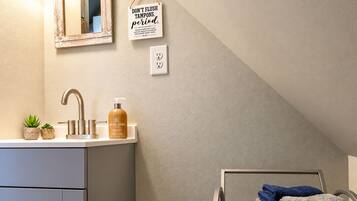 A bathroom with a sink, a mirror, a towel rack, and a wall-mounted sign.